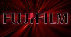 A glowing red background with the bold, uppercase text "FUJIFILM" displayed prominently in black with white outlines. A stylized design in white and red is used for the "J" in "FUJIFILM". Radiating lines give a dynamic effect to the background.