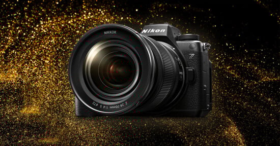 A Nikon camera with a large lens is displayed against a glittering gold background. The camera has a prominent Nikon logo and a Z series mark, indicating it is part of Nikon's Z series lineup. The lens reads "NIKKOR 24-70mm.