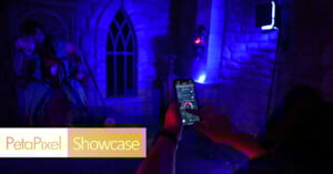 A person using a smartphone to photograph a haunted house scene with two eerie figures in a dimly lit, blue-toned room. the photo features a prominent "petapixel showcase" watermark.